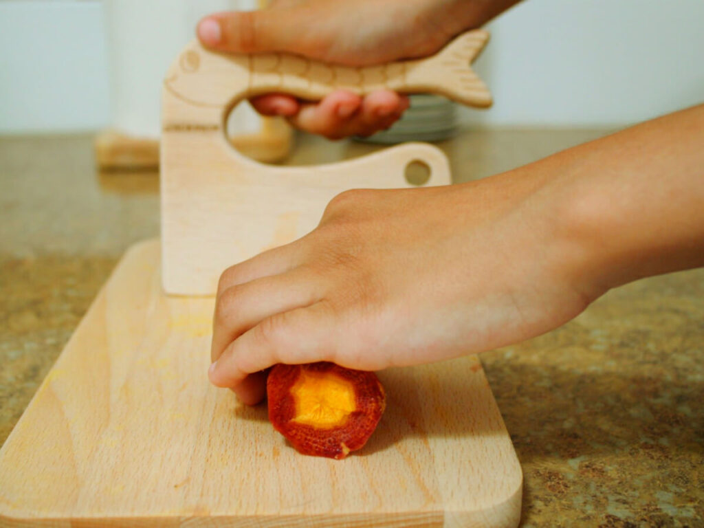 Child slicing carrot into coins with a kid-safe knife on a cutting board