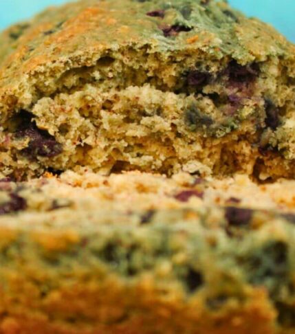 Close-up of Vegan Blueberry Lemon Loaf with one slice cut, showing juicy blueberries and golden crust.