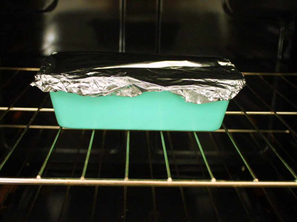 Loaf pan of vegan vegetable lasagna covered with foil baking in oven