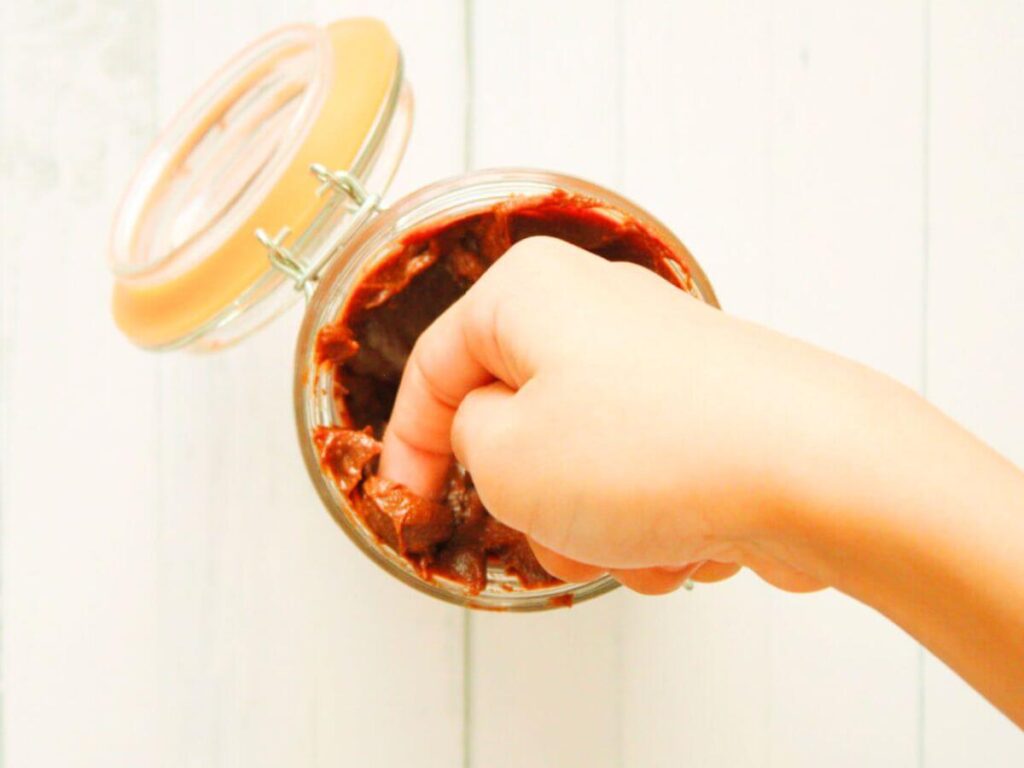 Child dipping a finger into a jar of vegan chocolate hazelnut spread for a taste