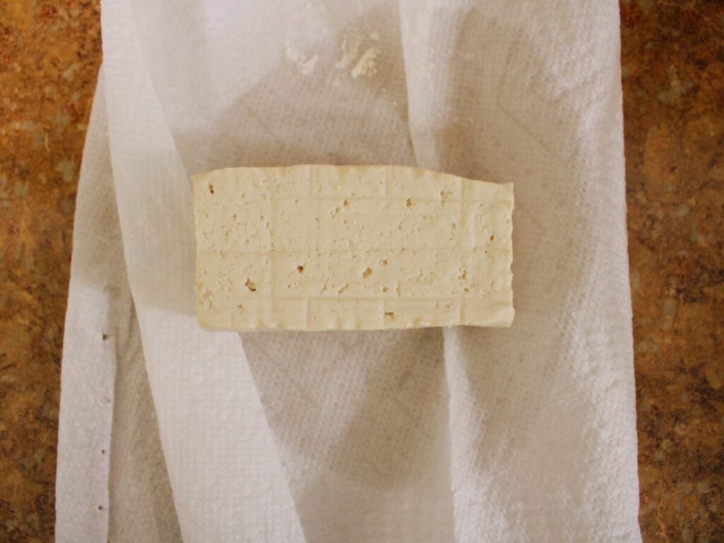 Block of tofu on paper towels ready to be crumbled for vegan scrambled eggs.