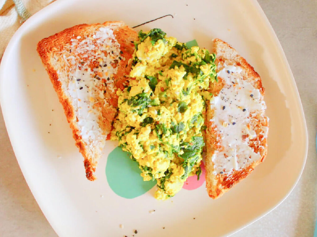 Vegan scrambled eggs made from tofu served with toast and topped with chopped spinach.
