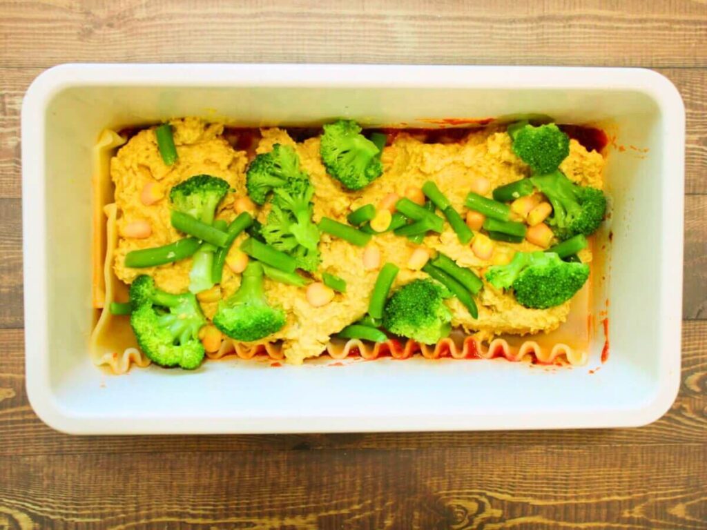 Broccoli florets and corn kernels added to cheese layer while making vegan vegetable lasagna