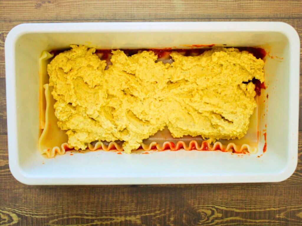 Vegan cheese layer spread over lasagna noodles in pan for vegan vegetable lasagna