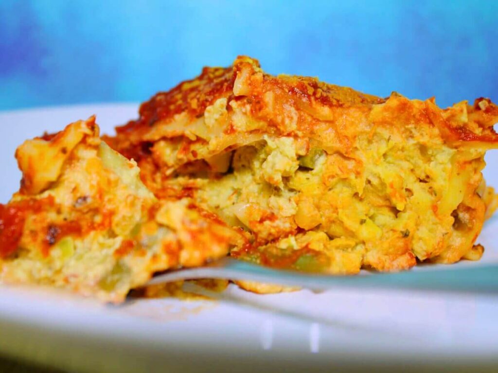 Fork lifting a bite of kid-friendly vegan vegetable lasagna showing layers of noodles and vegetables