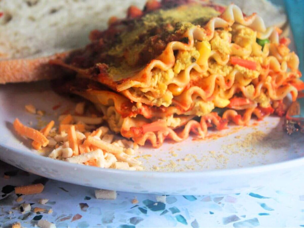 Side view of layered vegan vegetable lasagna slice on plate with bread