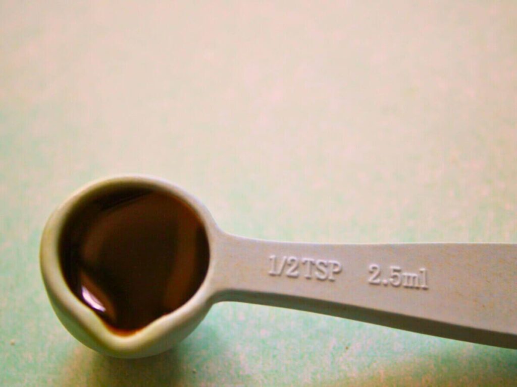 Half teaspoon of vanilla extract being measured for blueberry vegan donuts