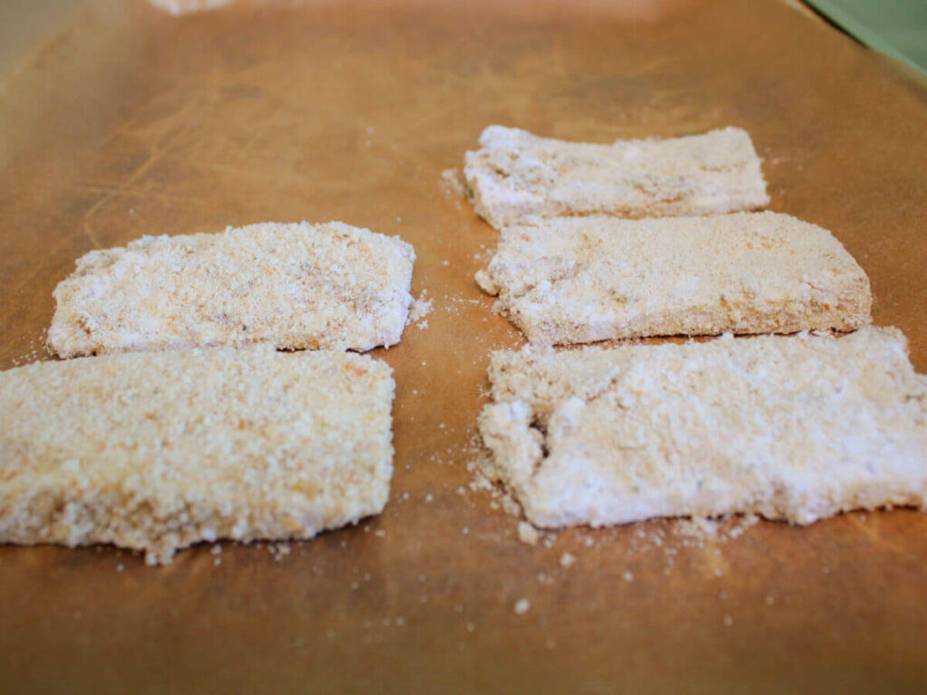 Breaded vegan turkey cutlets on parchment paper ready to bake in the oven.