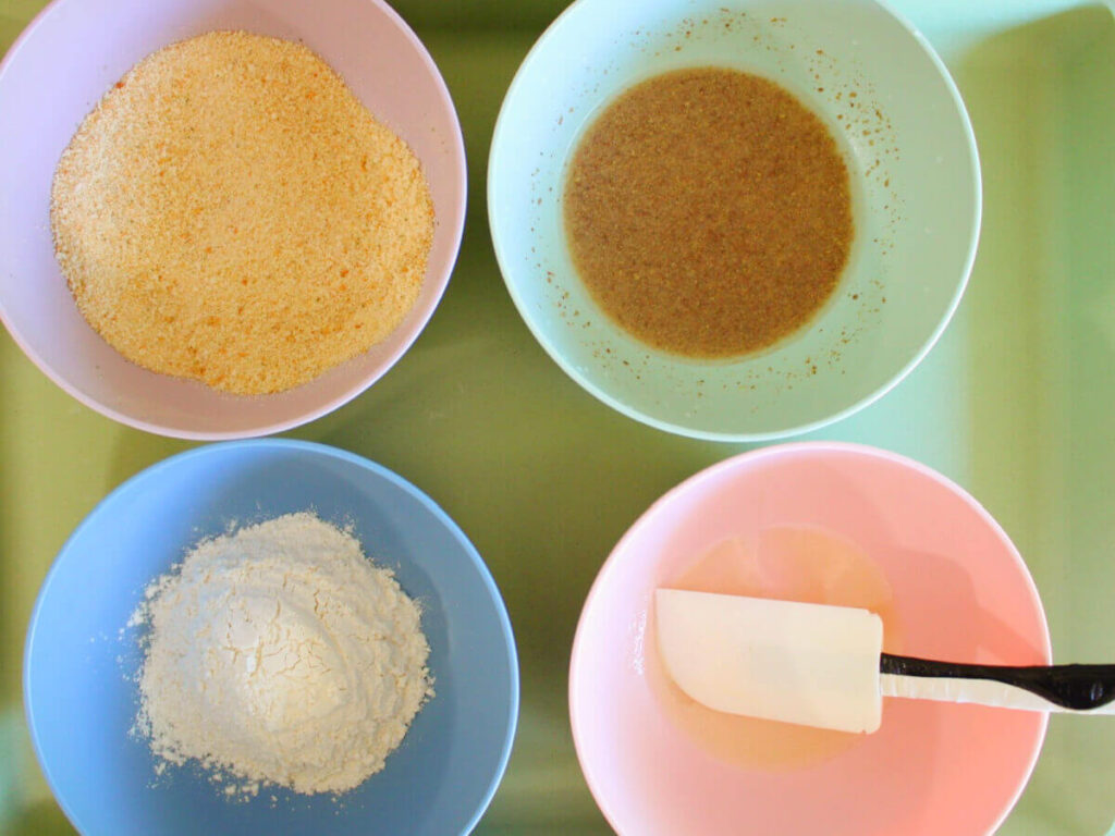 Four bowls with flour, flax egg, breadcrumbs, and melted butter for breading vegan turkey cutlets.