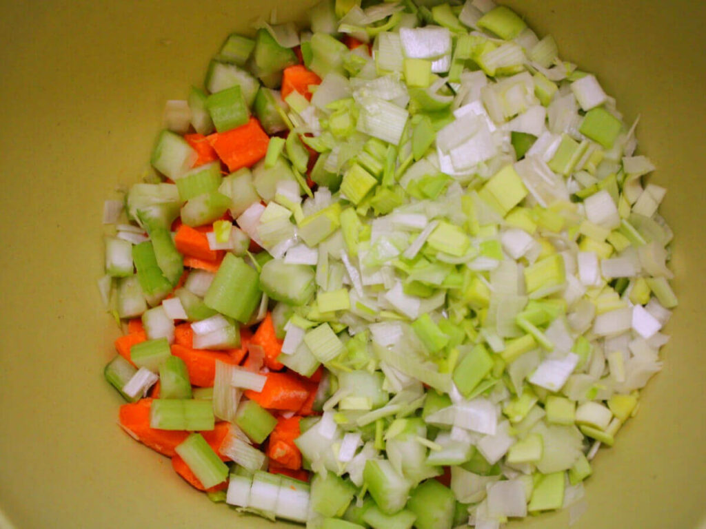 Overhead view of diced leeks, carrots, and celery in a bowl prepared for kid-friendly vegan vegetable soup