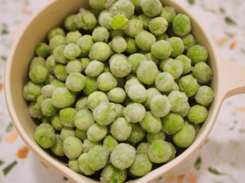 Overhead view of frozen peas in a measuring cup for kid-friendly vegan vegetable soup