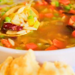 Close-up of kid-friendly vegan vegetable soup with carrots, peas, kidney beans, and celery on a spoon