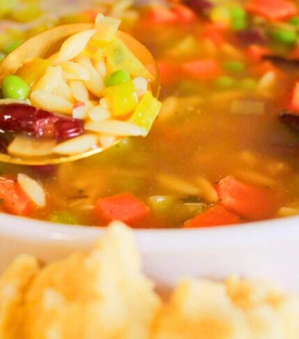 Close-up of kid-friendly vegan vegetable soup with carrots, peas, kidney beans, and celery on a spoon