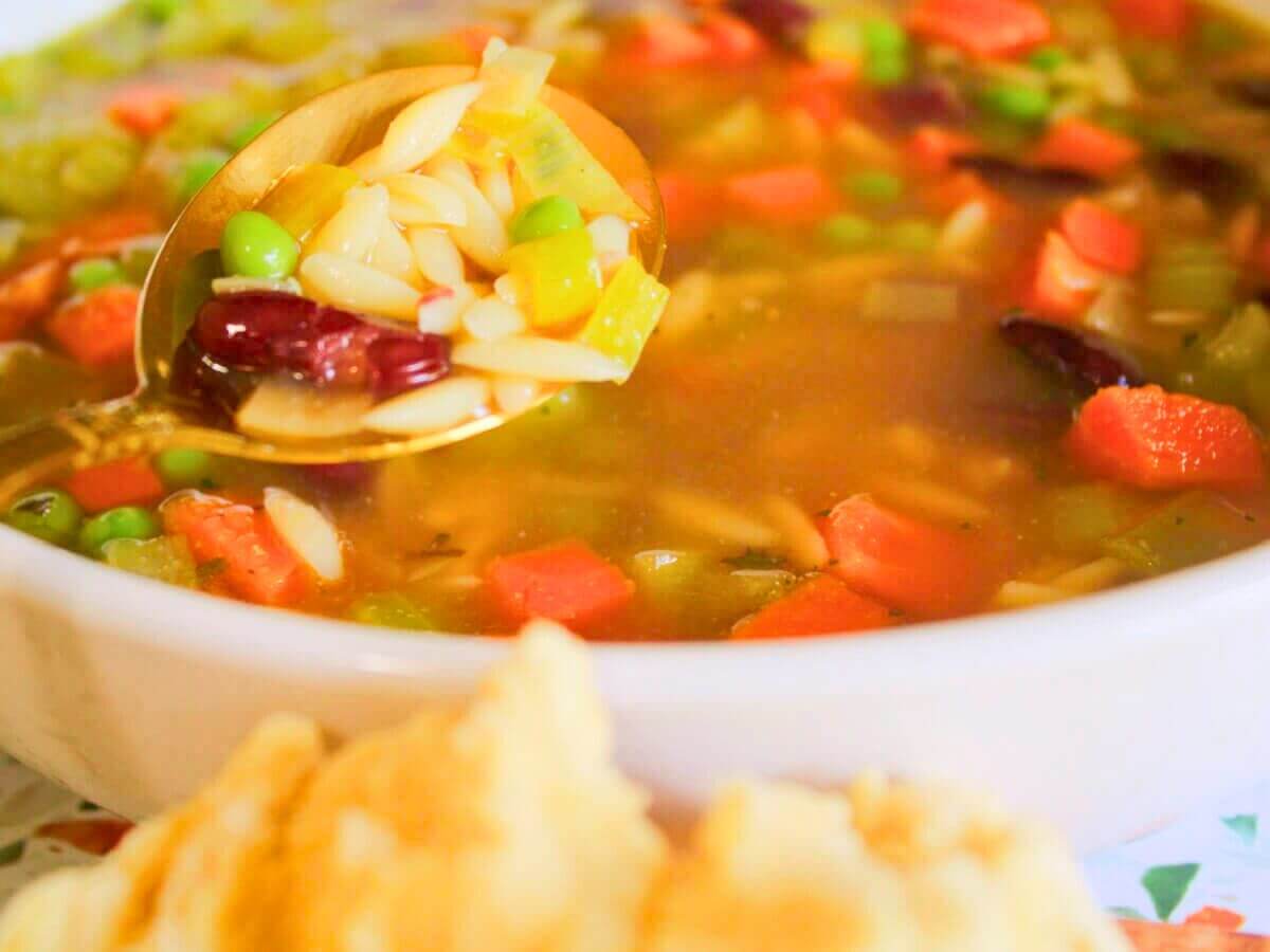 Close-up of kid-friendly vegan vegetable soup with carrots, peas, kidney beans, and celery on a spoon