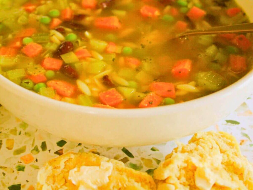 Bowl of kid-friendly vegan vegetable soup with a spoon and a buttered biscuit on a plate