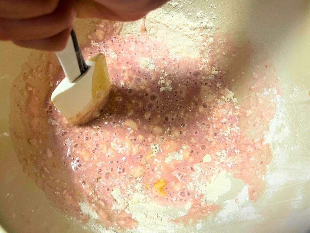 child’s hand mixing flour and strawberry milk to make vegan pancake batter