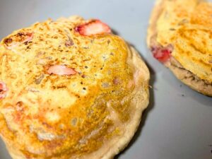 two golden vegan pancakes cooking in a pan, almost ready to flip