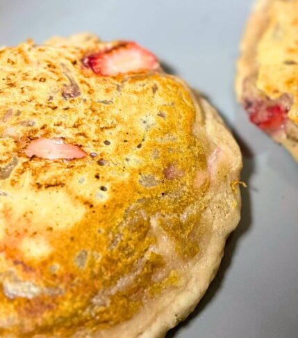 two golden vegan pancakes cooking in a pan, almost ready to flip