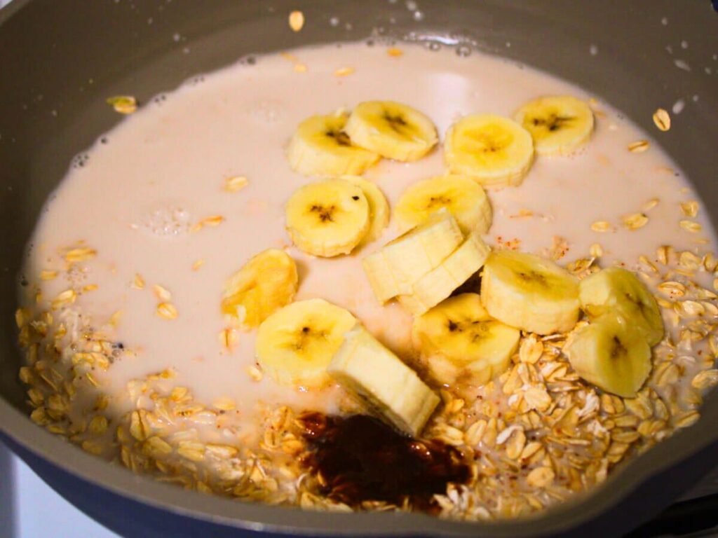 Rolled oats, sliced banana, plant-based milk, nutmeg, and vanilla in a pot before cooking