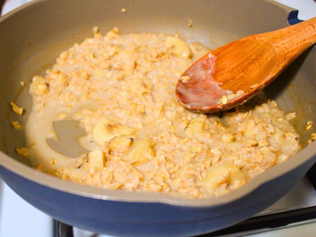 Healthy vegan fall oatmeal thickening in a pot on the stove as bananas melt into the oats