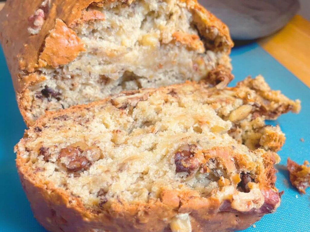 Whole loaf of vegan banana bread with one slice cut on wooden board