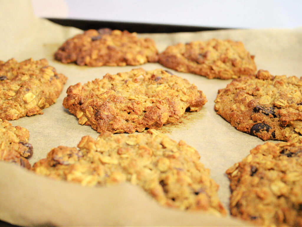 Golden brown banana bread breakfast cookies cooling on parchment paper on a black baking sheet