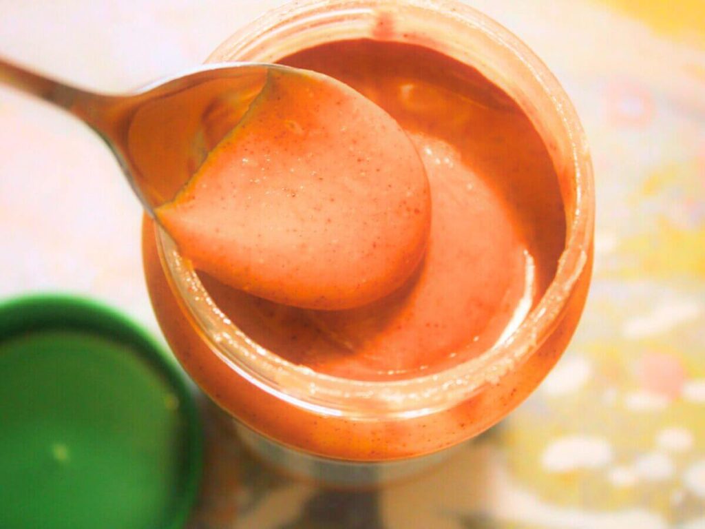 Overhead view of a spoonful of creamy peanut butter held over an open jar of peanut butter