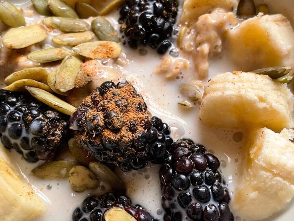 Finished vanilla overnight oats for kids topped with fresh blackberries, chopped walnuts, and a light dash of nutmeg in a glass jar