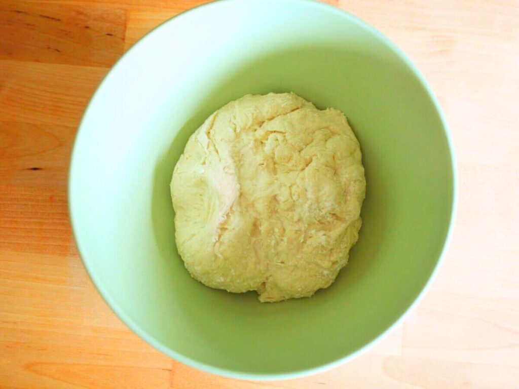 Ball of healthy vegan pizza dough resting in a mixing bowl before baking