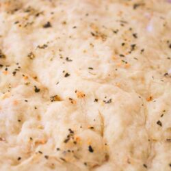 Close up of healthy vegan pizza dough brushed with garlic butter and topped with fresh herbs before baking