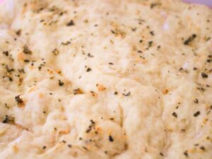 Close up of healthy vegan pizza dough brushed with garlic butter and topped with fresh herbs before baking