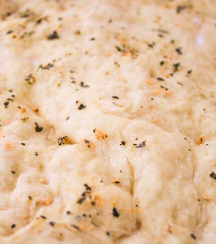Close up of healthy vegan pizza dough brushed with garlic butter and topped with fresh herbs before baking