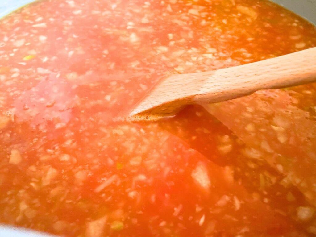 vegan tomato rice soup cooking in pot with wooden spoon