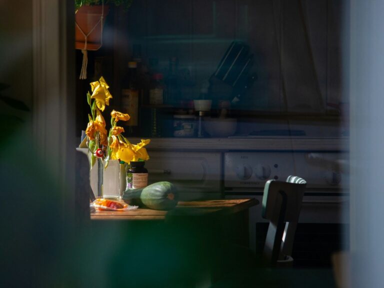 A dark American kitchen with light illuminating a table of fresh food and flowers, symbolizing a return to home cooking