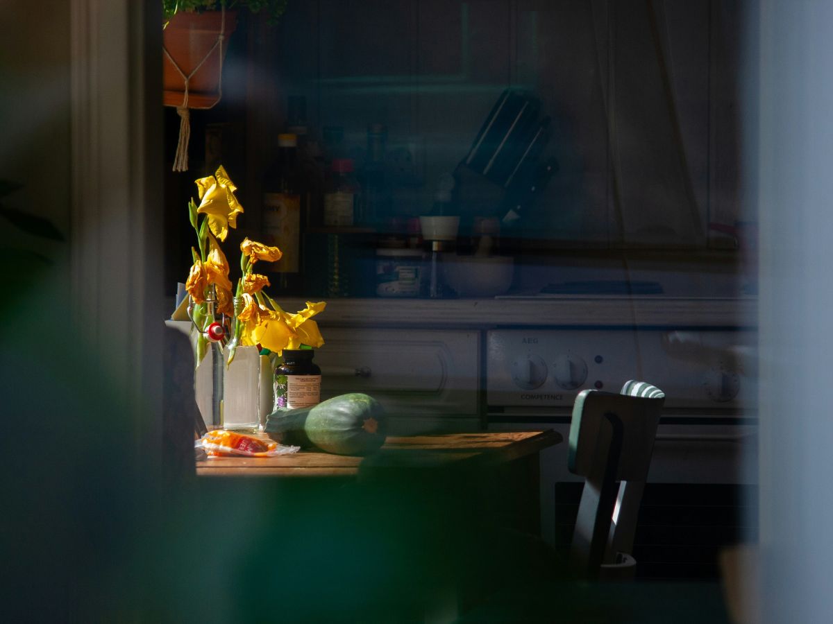A dark American kitchen with light illuminating a table of fresh food and flowers, symbolizing a return to home cooking