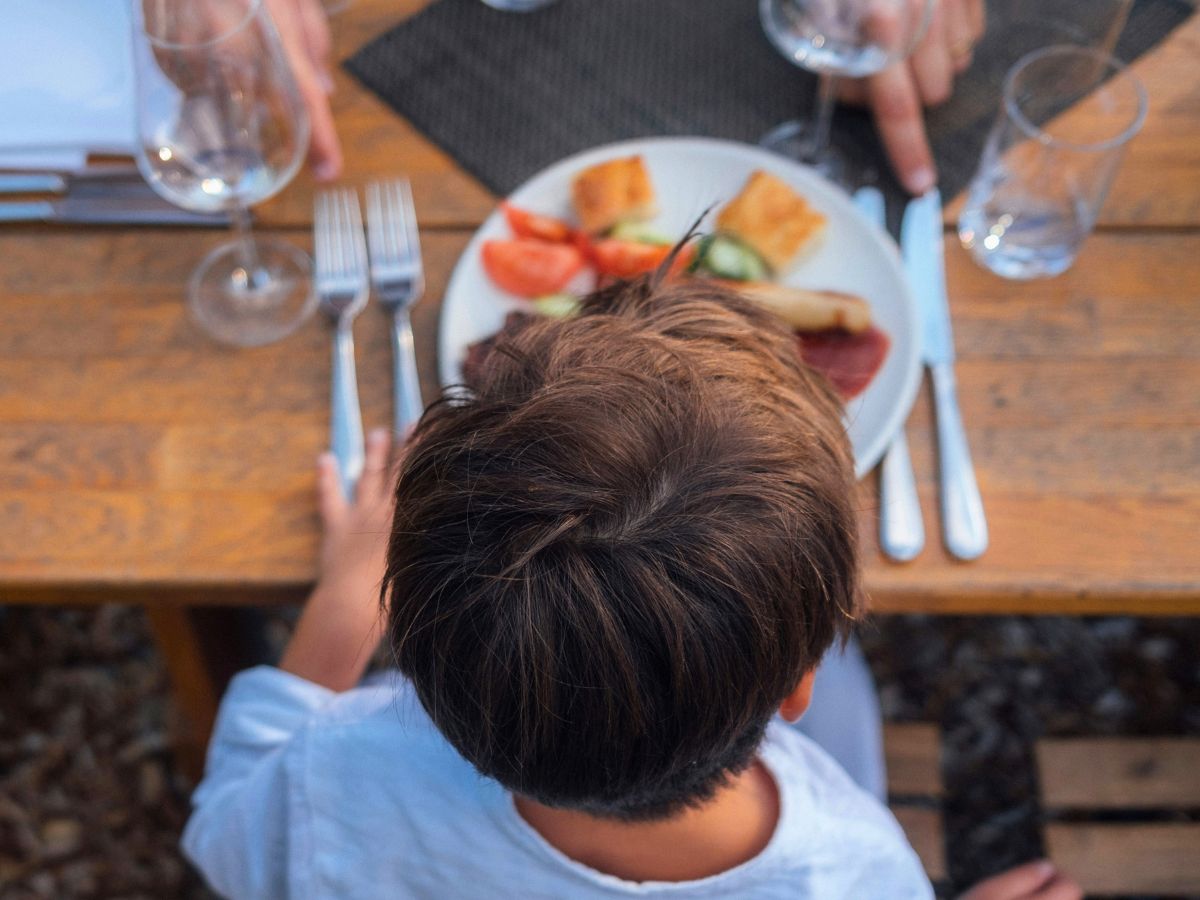 child sitting at dinner table with parent guiding meal