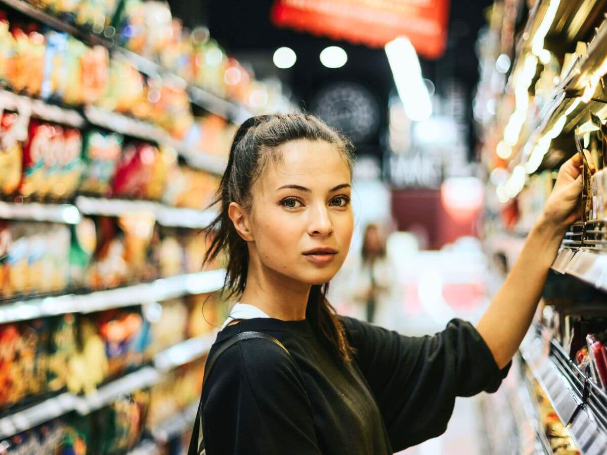 Person standing in grocery store aisle looking uncertain about food choices and products