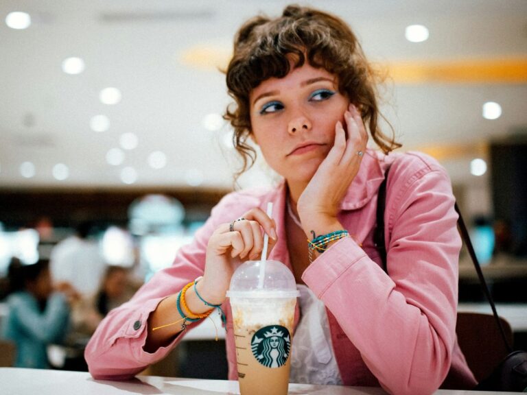 A person sitting at a Starbucks counter with a concerned expression next to a cold Frappuccino