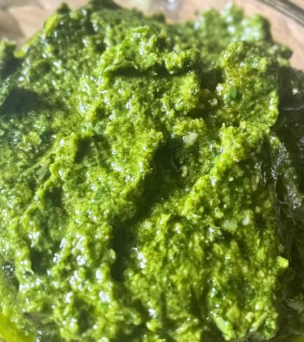 Vegan basil pesto in a round glass container, smooth and bright green