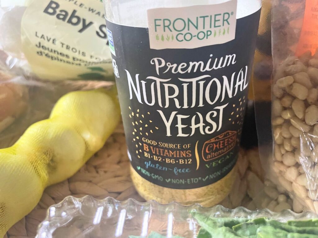 Ingredients for vegan basil pesto including basil garlic olive oil nuts and nutritional yeast on table