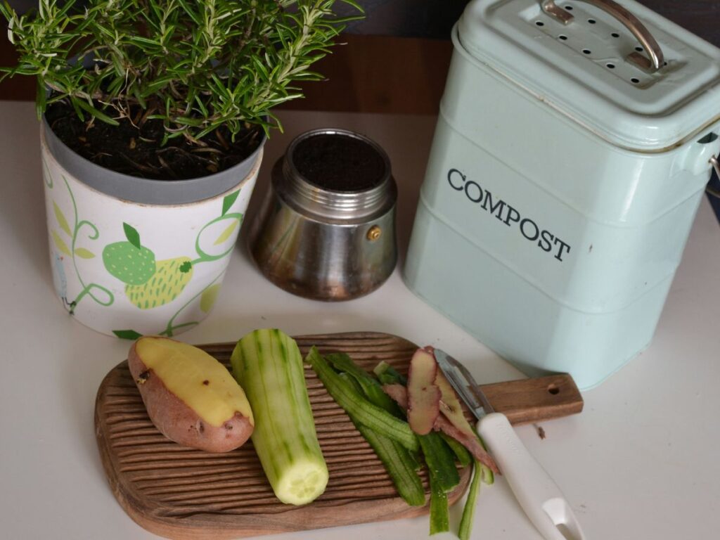 Vegetable scraps on a cutting board next to a compost bin and fresh herbs, showing food waste reduction in a home kitchen
